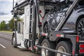 Powerful white big rig car hauler industrial semi truck transporting cars on the two levels hydraulic semi trailer running on the Royalty Free Stock Photo