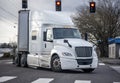 Powerful bonnet white big rig semi truck with dry van semi trailer turning on the city street crossroad with traffic light and Royalty Free Stock Photo