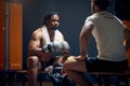 Powerful boxer in sweats resting on bench after workout, talking with his coach, getting consultation