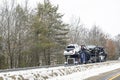 Powerful classic blue big rig car hauler semi truck transporting pick up trucks on the modular semi trailer driving on the winter