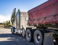 Powerful classic gray big rig semi truck transporting covered and tightened cargo on the flat bed semi trailer running on the Royalty Free Stock Photo