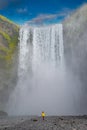 Powerful and famous Skogafoss waterfall with a lonely standing person in orange jacket, while hiking in Iceland, summer, scenic