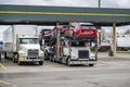 Powerful industrial big rig semi trucks with dry van and car hauler loaded semi trailers standing on the truck stop parking lot