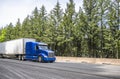 Powerful industrial long haul blue big rig semi truck transporting goods in dry van semi trailer running on the wide highway road Royalty Free Stock Photo