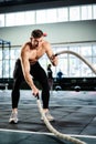 powerful man training battle ropes at cardio workout in dark gym. Professional athlete exercise fitness sport club equipment. Royalty Free Stock Photo