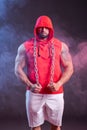 Powerful muscular man with a hood and chain posing in the red sweatshirt. Studio shoot with red and blue smoke