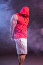 Powerful muscular man with a hood posing in the red sweatshirt. Studio shoot with red and blue smoke