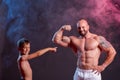 Powerful muscular man shirtless posing with his son in the studio with red and blue smoke. Little boy showing biceps contraction Royalty Free Stock Photo