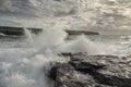 Powerful ocean wave crushes on rock, cliff with green fields and blue cloudy sky in the background. Beautiful nature scenery. Royalty Free Stock Photo