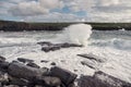 Powerful ocean wave crushes on rock, cliff with green fields and blue cloudy sky in the background. Beautiful nature scenery. Royalty Free Stock Photo