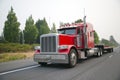 Powerful red big rig semi truck with flat bed step down semi trailer move on smog road for loading cargo