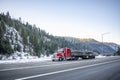 Powerful red classic big rig semi truck transporting industrial cargo on the long flat bed semi trailer climbing uphill on the