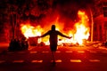 Epic powerful scene of young catalan protester walking against huge fire with arms wide open in the background at night during