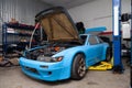A powerful tuned blue sports car with an open hood and a powerful engine stands on a lift in a workshop for repair and maintenance