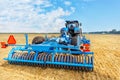 A powerful universal blue harrow on an agricultural tractor against the background of a harvested yellow wheat field