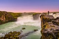 Powerful waterfall Godafoss at beautiful red sunset with a lonely traveler standing at its cliff, Iceland, summer, scenic view