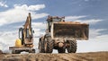 Powerful wheel loader or bulldozer working and mini excavator against blue cloudy sky. Modern equipment for earthworks. Rental of Royalty Free Stock Photo