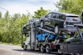 Powerful white big rig car hauler semi truck transporting cars on the two level modal semi trailer running on the road with trees