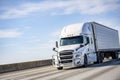 Powerful white big rig long haul industrial semi truck transporting goods in refrigerator semi trailer driving on the sunny Royalty Free Stock Photo