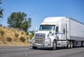 Powerful white big rig semi truck with grille guard transporting cargo in dry van semi trailer running on the summer highway road Royalty Free Stock Photo