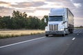 Powerful white big rig semi truck with turned on headlight transporting cargo in dry van semi trailer running on the evening Royalty Free Stock Photo