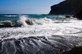 Powerful white foaming waves hit black lava sand beach in the evening sun