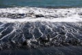 Powerful white foaming waves hit black lava sand beach in the evening sun