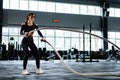 Powerful woman training battle ropes at cardio workout in dark gym. Professional athlete exercise fitness sport club equipment. Royalty Free Stock Photo