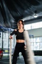 Powerful woman training battle ropes at cardio workout in dark gym. Professional athlete exercise fitness sport club equipment. Royalty Free Stock Photo