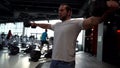 Powerlifter or bodybuilder is training in gym, man is lifting dumbbells by hands, tensing muscles