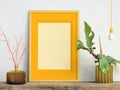 Yellow mock up picture frame on white plaster wall with plant in golden pot and glass vase with branches on wooden shelf, 3D illus Royalty Free Stock Photo