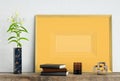 Golden mock up picture frame on white plaster wall with lily flower in marble vase, books, geometric sculpture and vase, 3d illust