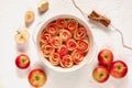 ÃÂpple rose tart in the baking dish decorated with fresh sliced apples and cinnamon sticks. Vegetarian autumn pie on white table Royalty Free Stock Photo