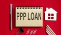 PPP LOAN text written on a notebook with pencils and office tools and model wooden house Royalty Free Stock Photo