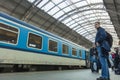 A guy waiting for the train at the Prague main train station with people boarding the blue train of Ceske Drahy