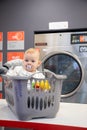 Prague, Czech Republic - 16.12.2020: Baby girl in plastic basket waiting in laundry room with Speed Queen self service