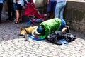 An elderly man with a black beard kneels and begs for alms