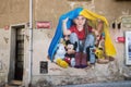 Graffiti by Chemis artist depicts a little girl hiding a European fairy tale character under a blanket from Ukrainian flag
