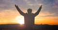 Praise and worship concept: Silhouette human raising hands to praying God on blurred cross with crown of throne sunset background Royalty Free Stock Photo