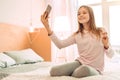 Upbeat teenage girl taking selfie on bed