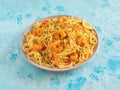 Prawn Schezwan Noodles with vegetables in a plate on a blue table