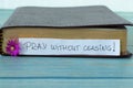 Pray without ceasing, a handwritten text on a note with a purple flower in front of a closed Holy Bible Book on wood
