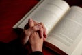 Pray to God. Female hand in prayer over a Holy Bible, wooden table, close up view Royalty Free Stock Photo