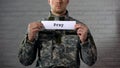 Pray word written on sign in hands of male soldier, serviceman asking for peace