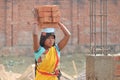 A poor female construction worker carrying heavy bricks on her head.