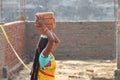 A rural female construction worker carrying heavy bricks with her hands over head.