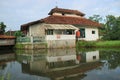 A prayer room building standing in the middle of rice fields and directly adjacent to a fish pond