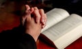 Pray to God. Female hand in prayer over a Holy Bible, wooden table, close up view Royalty Free Stock Photo