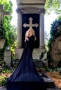 praying mature redhead woman with curls in black robe in front of a tombstone with historical christian cross at vienna central