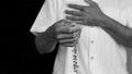 Praying rosary concept with man holding rosary beads in hand and another hands on chest in black and white background. Royalty Free Stock Photo